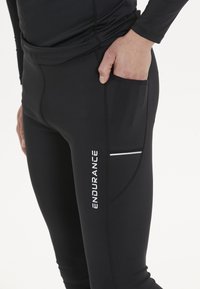Svarta atletiska leggings med en sidficka, reflexdetaljer och tryckt logga på låret. Slätt, elastiskt tyg.