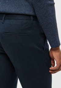 Marinblå bomullsbyxor med smal passform, med en bakficka och diskret branding, kombinerade med en figurnära ribbad marinblå tröja.