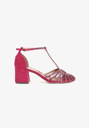 Fuchsia ruskindsandal med blokhæle, der har en T-remslukning, åben tå og udskæringsdesign med metaldetaljer langs oversiden.