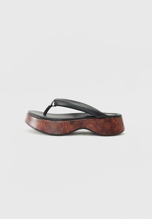 Chinelo preto com uma tira de couro texturizado, plataforma de madeira contornada e design de sola curvada. Padrão de madeira notável na base.