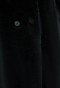 Palton din blană sintetică neagră, cu două butoane rotunde negre, textură netedă și finisaj moale. Design simplu, cu o formă elegantă.
