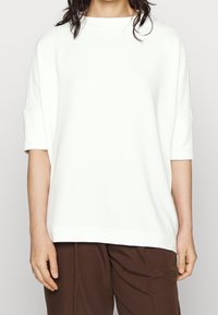 Biały, prążkowany, luźny top z krótkimi rękawami i okrągłym dekoltem, w połączeniu z brązowymi spodniami. Gładka tekstura i luźny krój.