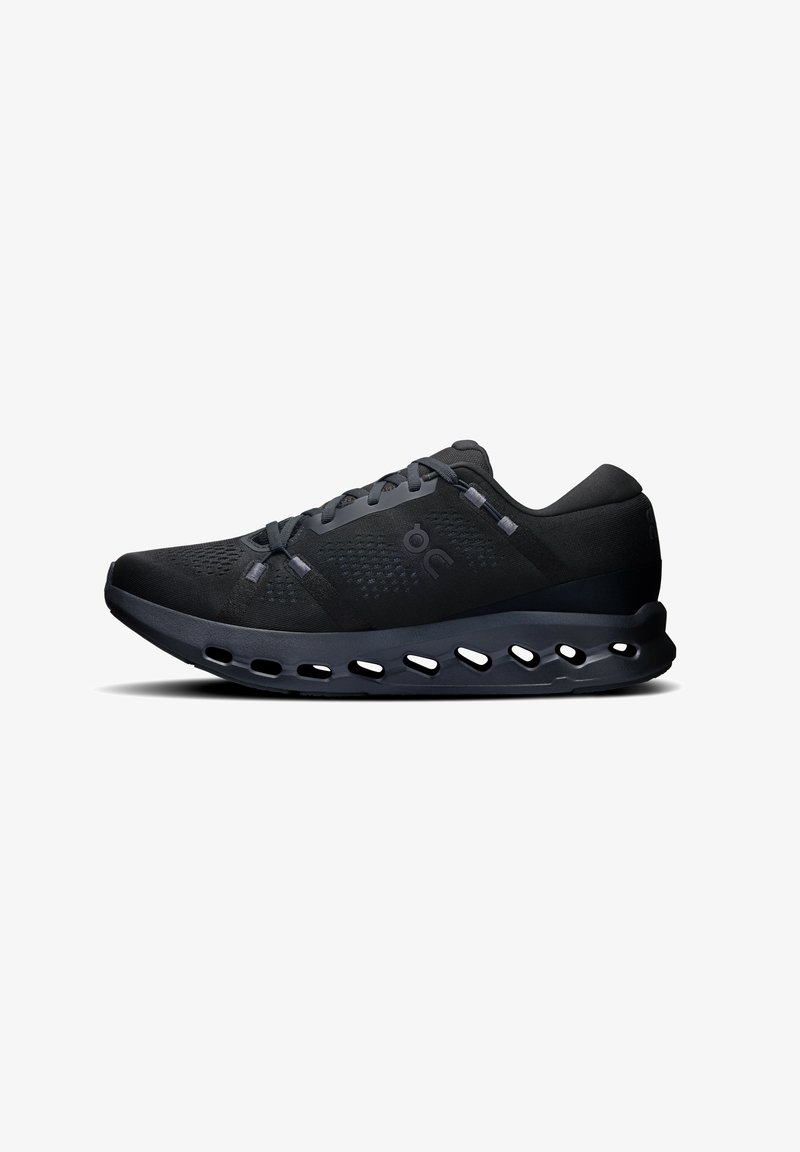 Baskets de sport noires avec une tige en maille, des découpes circulaires dans la semelle et un design épuré. Caractéristiques d'un embout renforcé et de lacets plats.