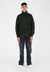 Maglione a collo alto lavorato a maglia verde scuro, vestibilità comoda, polsini e orlo a coste, abbinato a jeans neri sbiaditi e sneakers bianche.