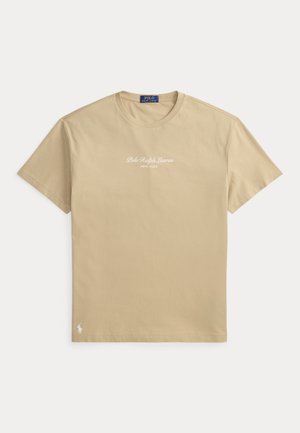 Μπεζ κοντομάνικη μπλούζα Polo Ralph Lauren με στρογγυλή λαιμόκοψη, λευκό τυπωμένο λογότυπο "Polo Ralph Lauren New York" στο στήθος και μικρό λογότυπο κοντά στο τελείωμα.