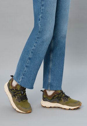 Sneakers verdi e grigi con tessuto texturizzato, lacci e fodera in pelliccia. Suola spessa maculata. Abbinati a jeans dritti blu chiaro.