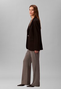 Sort blazer med hakkede revers, enkelt knaplukning, kombineret med lysegrå bukser med vide ben og spidse sorte sko, glat stof.