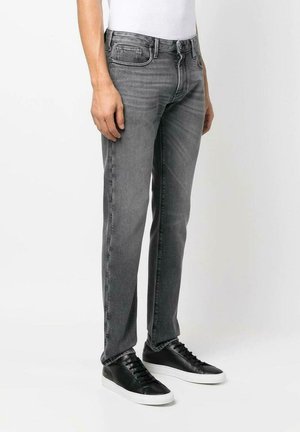 Jeans in denim grigio con vestibilità slim, design a cinque tasche e passanti per cintura, abbinati a sneakers nere con suola bianca.