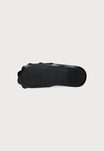 Chaussure noire vue de dessous, révélant une semelle extérieure lisse et plate avec des bords légèrement ondulés et une section de talon définie.