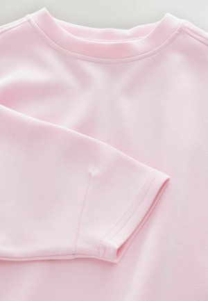 Jasnoróżowa bluza z okrągłym dekoltem, długimi rękawami i gładką fakturą z widocznymi detalami ściegów.
