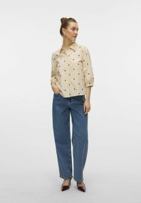 Beige skjorta med knappar och röd hjärttryck, med samlade ärmar, i kombination med lösa blå jeans och burgundy högklackade skor.