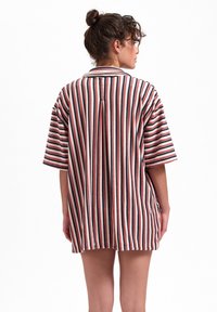 Gestreifte übergroße Bluse in cremigem Weiß, Rot und Marineblau. Sie hat kurze Ärmel, einen Schlitzausschnitt im Rücken und ein entspanntes Design.