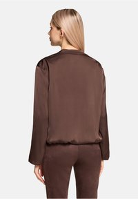 Brown satin blouse with long sleeves, a straight cut, and a smooth texture, featuring a rounded neckline and subtle stitching details.