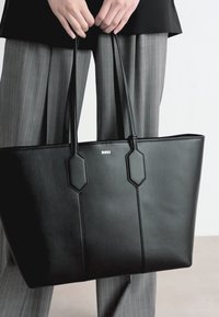 Melna ādas tote soma ar strukturētu dizainu, sešstūra akcentiem un sudraba "BOSS" logotipu. Iespējo divas garas rokturi un gludu tekstūru.