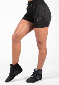 Zwarte sportshorts met elastische tailleband en zijzakken. Vergezeld van zwarte hoge sneakers met textuurpanelen en veters.