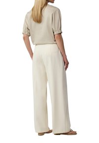 Hellbeige Bluse mit kurzen Ärmeln und gerafften Bündchen, kombiniert mit lockeren, cremefarbenen, weit geschnittenen Hosen und schlichten Sandalen.