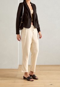 Černý blazer, béžový zkrácený top, krémové texturované kalhoty s šňůrkou a černé klínové pantofle. Viditelné minimalistické doplňky.