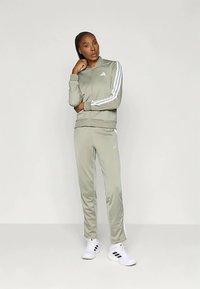 Fato de treino atlético em tecido verde claro, com riscas brancas nas mangas e nas calças. O modelo usa ténis brancos com detalhes em preto.