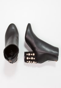 Schwarze Stiefeletten aus glattem Leder, mit spitzem Zeh und verziertem Blockabsatz, geschmückt mit perlähnlichen Nieten und metallischen Akzenten.