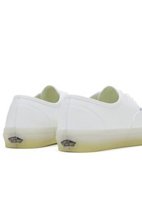 Een paar lage witte Vans sneakers met doorschijnende gelige zolen, gezien vanaf de achterkant tegen een witte achtergrond.