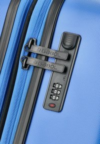 Equipaje texturizado azul con dobles cremalleras negras, un candado de combinación y un botón rojo. Presenta un material duradero y un diseño elegante.