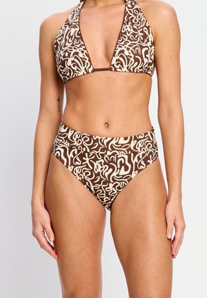 Femme portant un haut de bikini à motif abstrait marron et crème avec licou et un bas taille haute, debout devant un fond clair uni.