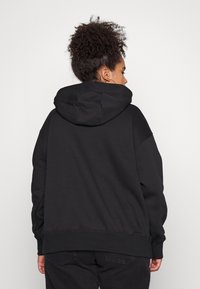 Čierna mikina s kapucňou, so voľným strihom, rebrovanými manžetami a spodným okrajom, a hladkou textúrou. Žiadne viditeľné logá ani vzory.