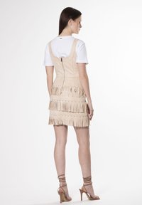 Vestido de flecos beige con cremallera trasera, que presenta detalles de flecos en capas en la falda y un corsé ajustado. Acompañado de tacones con tiras.