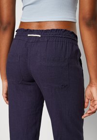 Pantalon bleu marine à coupe décontractée avec une taille élastique froncée, deux poches arrière et un simple logo. Texture de tissu douce et légère.