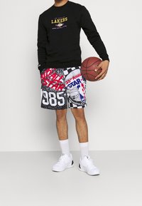 Sweat-shirt noir avec le logo "Los Angeles Lakers" ; short multicolore présentant des motifs graphiques, des chiffres et du texte ; baskets blanches.