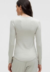 Lichtgrijze, lange mouw top met geribbelde textuur en een ronde onderrand. Heeft een eenvoudige ronde halslijn en minimaal stikseldetail op de achterkant.