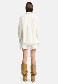 Hellblaue Denim-Hemd mit Knopfmanschetten, getragen über weißen, ausgefransten Shorts. Dazu gehören hohe, durchbrochene braune Stiefel mit spitzer Zehenform und Stiletto-Absatz.
