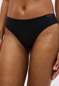 Κοντινό πλάνο ενός ατόμου που φοράει μαύρο μαγιό εσωτερικού τύπου Under Armour με ψηλή κοπή, εμφανίζοντας το κάτω μέρος του κορμού και το άνω μέρος των μηρών.