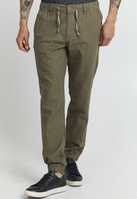 Olijfgroene joggerbroeken van lichte stof, met een elastische tailleband met trekkoord en elastische boorden. Gecombineerd met zwarte sneakers.