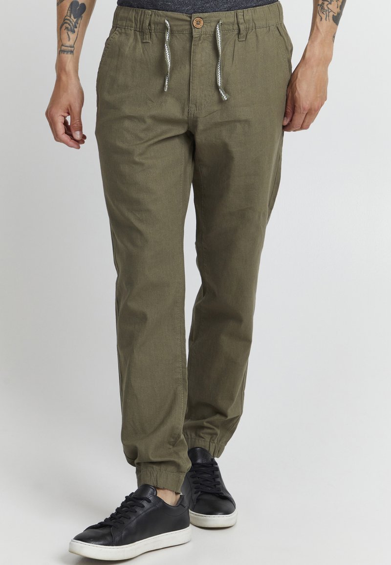 Olijfgroene joggerbroeken van lichte stof, met een elastische tailleband met trekkoord en elastische boorden. Gecombineerd met zwarte sneakers.