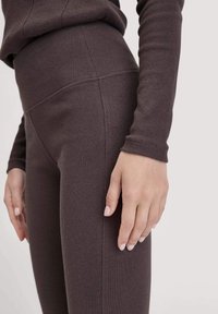 Donkerbruine geribde leggings met een hoge taille en een meetrekkende stof. De close-up toont de naaddetails en de tactiele uitstraling.