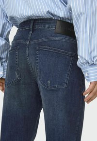 Dunkelblaue Jeans aus Denim mit glatter Textur, ausgestattet mit zwei Gesäßtaschen und einem schwarzen Lederetikett am Bund.