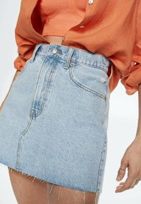 Minifalda de mezclilla azul claro con cintura alta, dobladillo deshilachado y dos bolsillos laterales. Presenta un cierre de botones en el frente y una cremallera.
