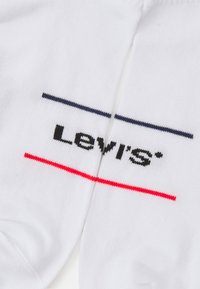 Bele bombažne nogavice z črnim logotipom "Levi's" in vodoravnimi črtami v mornarsko modri in rdeči barvi. Preprost, sproščen dizajn z mehkobo.
