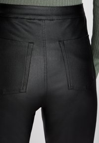 Calças pretas de cintura alta feitas de imitação de couro suave, com dois bolsos traseiros e um ajuste elegante. Costura mínima visível.