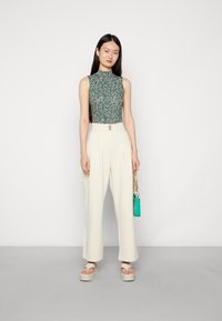 Bloemenromper in het groen met witte en roze patronen, witte hoge taille wijde pijpen broek, beige platform sandalen en een kleine turkooise tas.