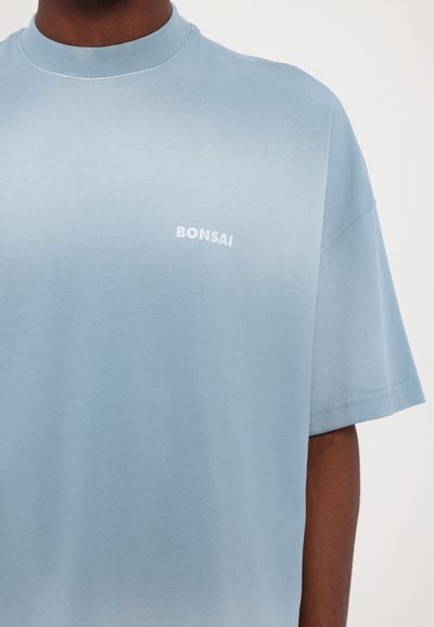 Debesszila kokvilnas T-krekls ar īsām piedurknēm, apaļas kakla izgriezums un balts "BONSAI" uzraksts kreisajā krūšu daļā.