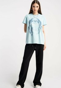 Jasnoniebieska bawełniana koszulka z nadrukiem graficznym, połączona z czarnymi spodniami w luźnym kroju. Strój ma swobodny fason i casualowy styl.