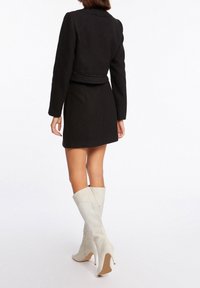 Musta teksturoitu takki yhdistettynä mustaan hameeseen. Valkoiset polven korkeudelle ulottuvat saappaat, jotka on valmistettu sileästä materiaalista, kärjessä ja korossa terävä muoto.