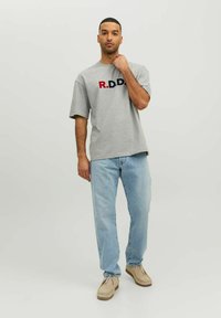 Šedé bavlnené tričko s krátkymi rukávmi, na ktorom je vyšitý nápis "R.D.D." v červenej a námorníckej modrej. Spárované so svetlo modrými džínsy a béžovými topánkami.