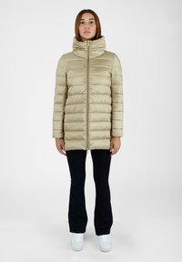 Giacca imbottita beige con colletto alto, cuciture orizzontali e zip frontale; abbinata a pantaloni neri e sneakers bianche.