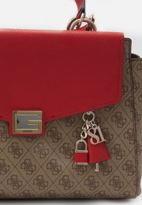Brączkowa torebka w wzory z czerwoną skórzaną klapą, srebrnymi elementami i ozdobnym zawieszką w kształcie zamka oraz etykietą z napisem "81".