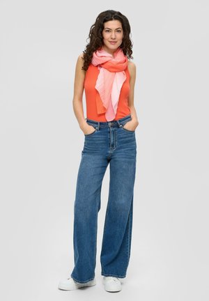 Orange sleeveless top, wide-leg blue jeans, and a pink gradient scarf with pleats, standing casually with hands in pockets.