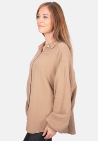 Khaki, lightweight button-up shirt with a textured fabric, collar, and loose-fitting long sleeves. Features a single button at the neckline.