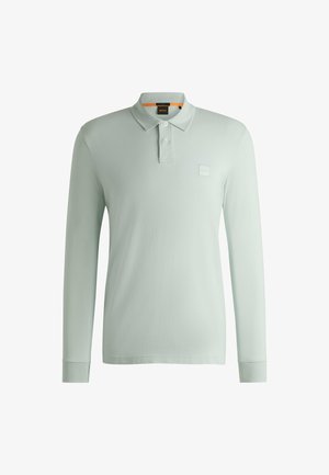 Lichtgroene polo met lange mouwen van zachte stof, voorzien van een klassieke kraag, drie knopen en een logopatch op de borst.